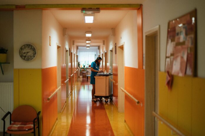Verpleegkundige met medicijnkar in lange zorggang, krappe bezetting in de zorg