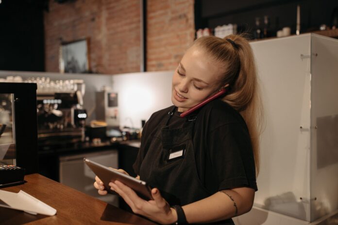 Barista met telefoon en tablet achter de toonbank, bij uitspraak gerechtshof over Temper en uitzendwerk